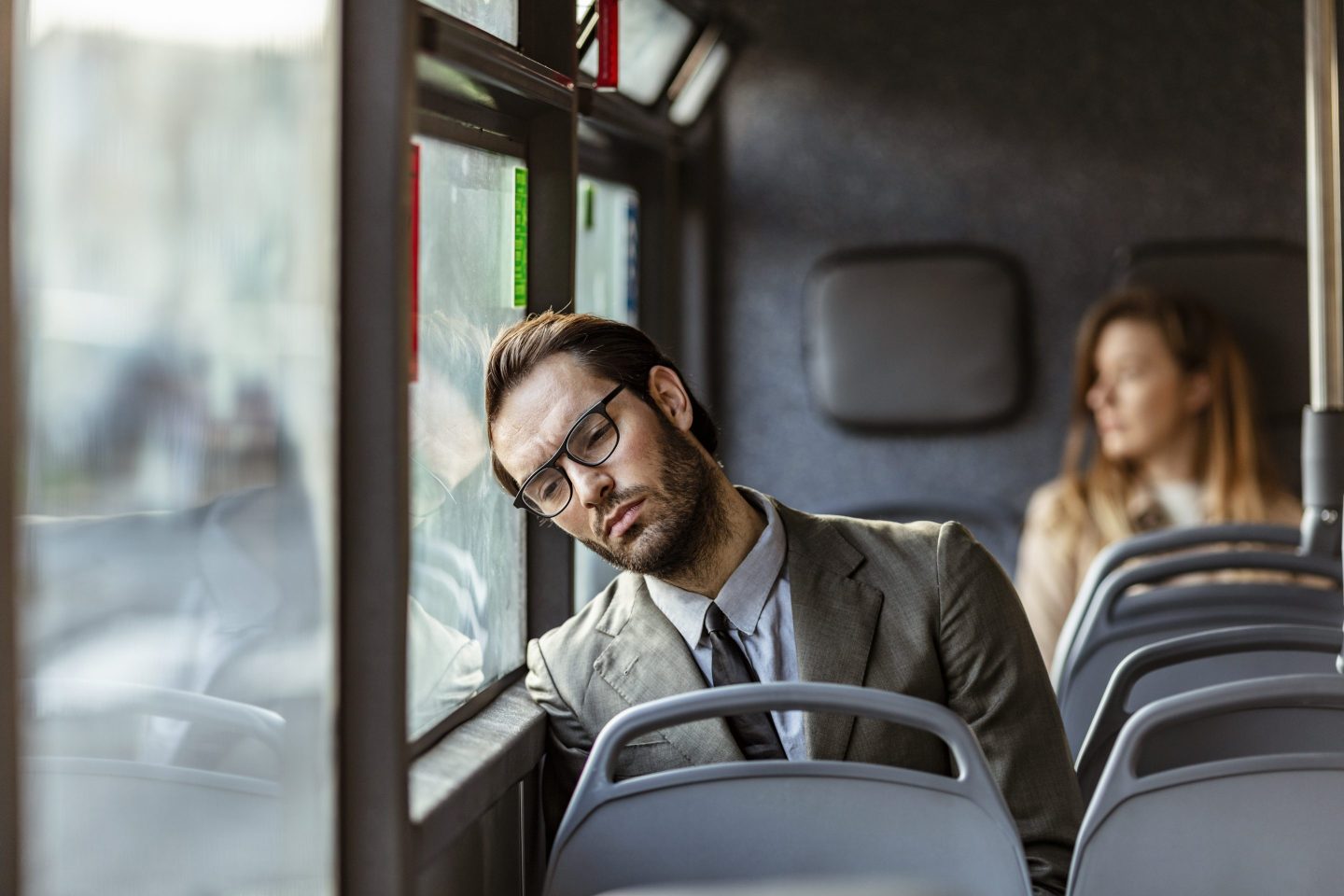 Tired young businessman sitting on the bus and day dreaming while leaning on the window during the day.