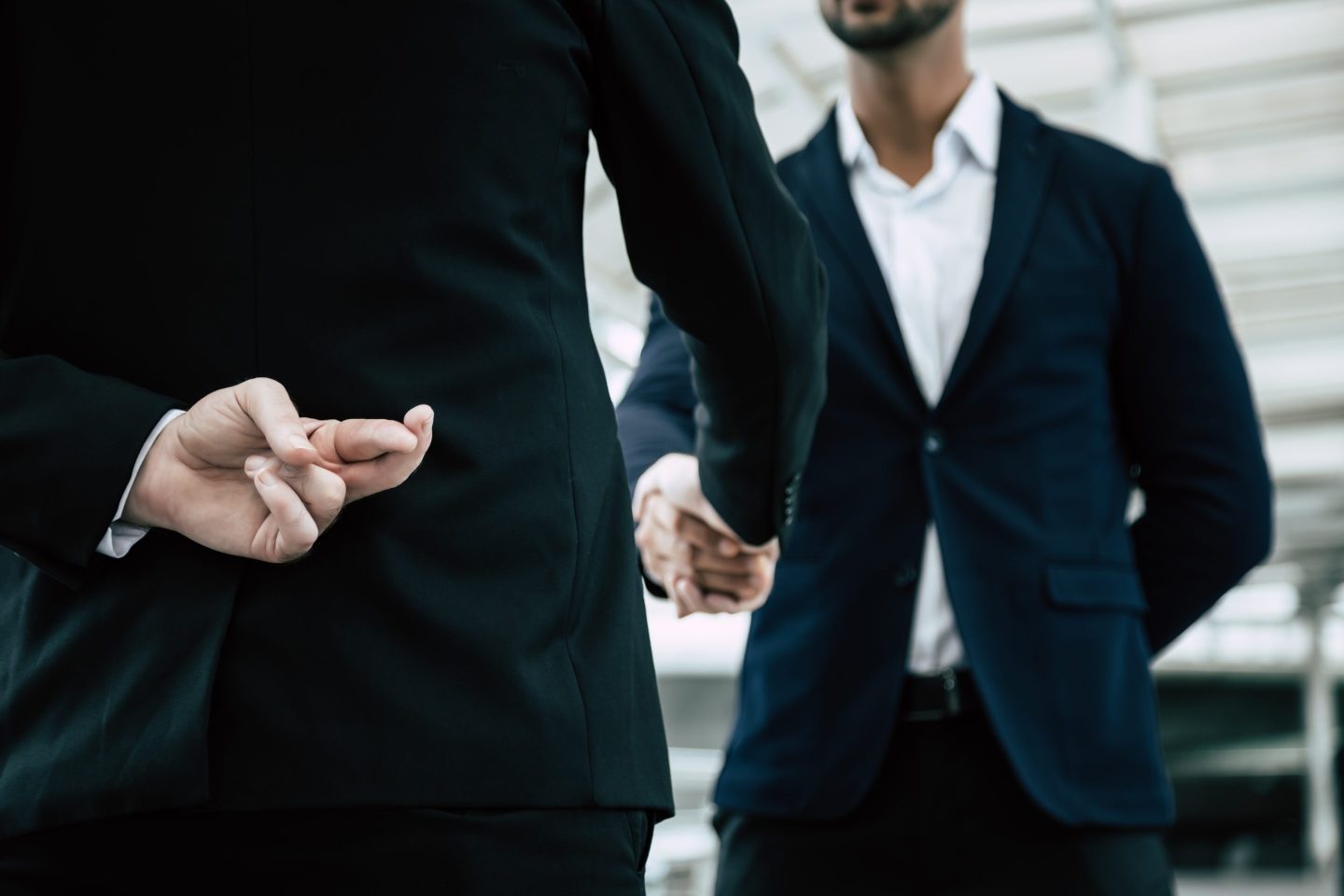 A man in a business suit crossing his fingers behind his back while he shakes another man's hand.
