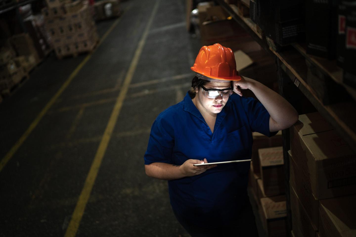 Woman in hard hat looks at a screen in a dark warehouse