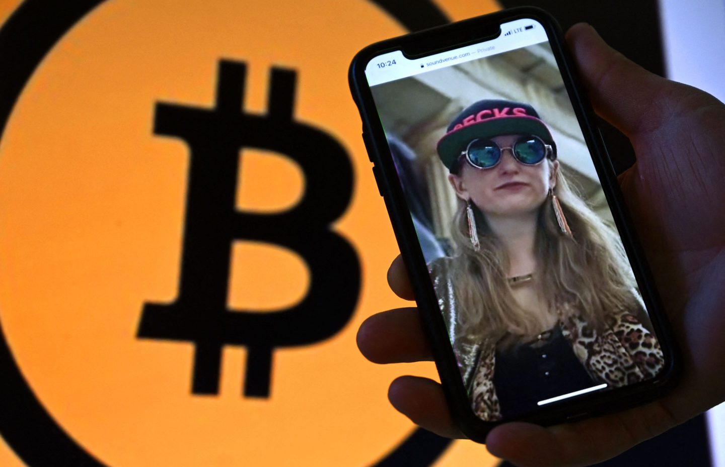 Heather Morgan, a.k.a. "the Crocodile of Wall Street,” on a phone in front of the Bitcoin logo displayed on a screen.