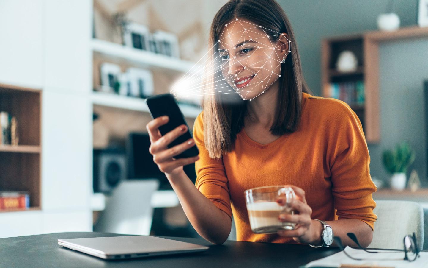 Facial recognition software scans the face of young woman holding smartphone at home.