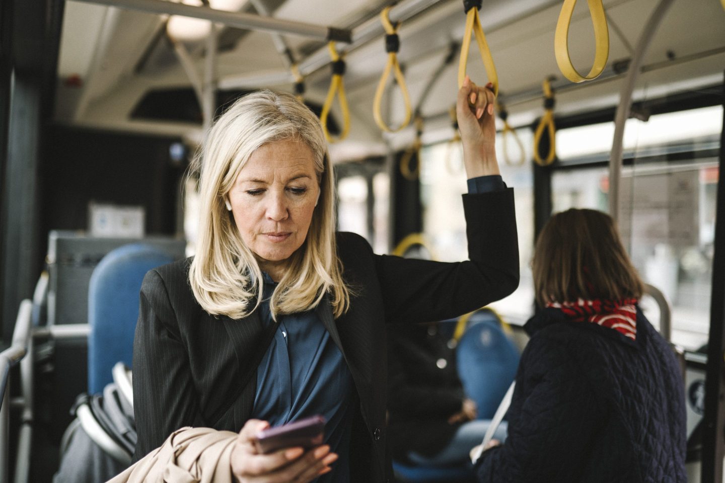 Businesswoman holding grab handle while using smartphone in bus