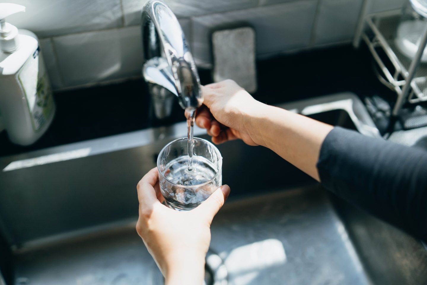 Cropped shot of woman's hand filling a glass of filtered water right from the tap in the kitchen sink at home