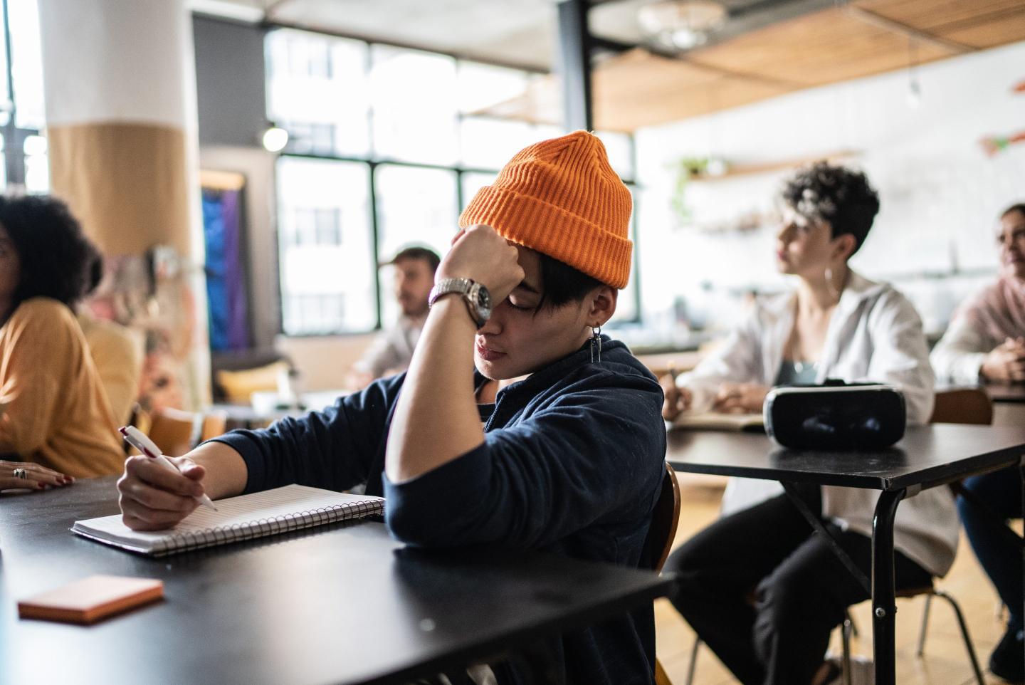 A tired young man takes notes during a college class.