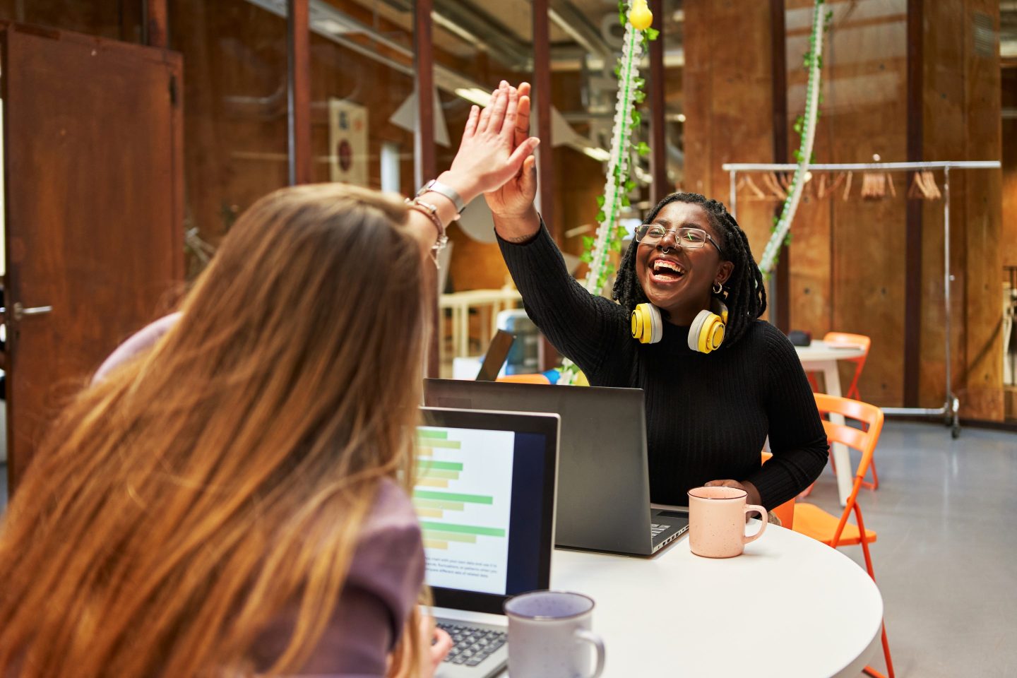 Two work colleagues giving each other high-five to express success while sitting at their workstations