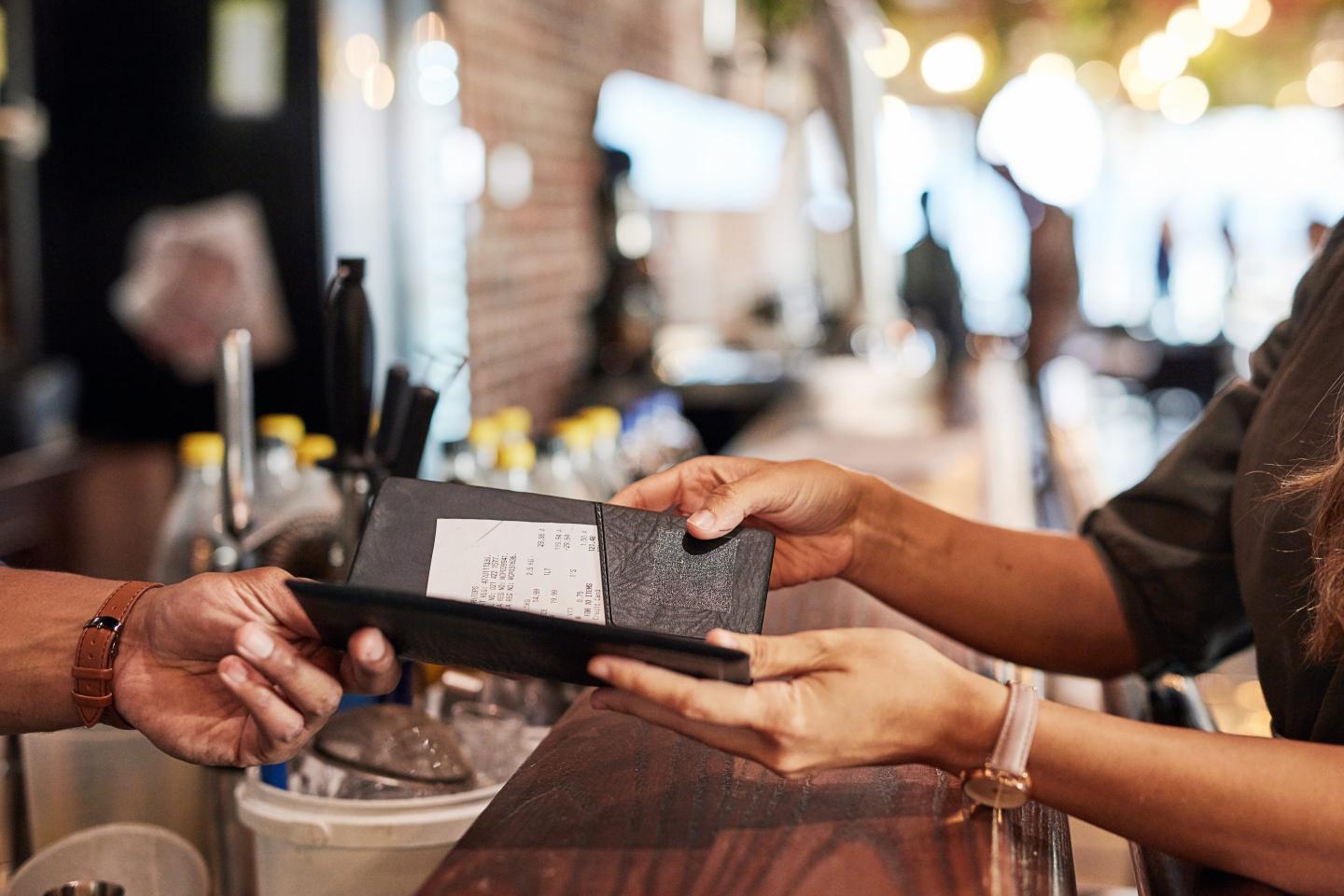 Two pairs of hands exchange a restaurant bill.