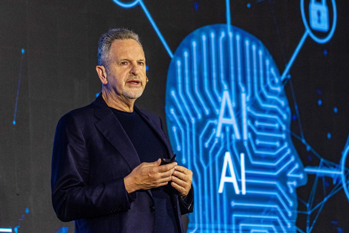 man in black shirt stands in front of screen with an "A.I." logo