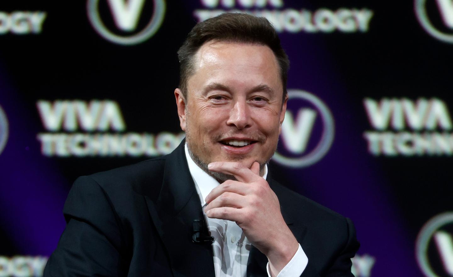 A picture of Elon Musk holding his hand to his chin and smiling slightly