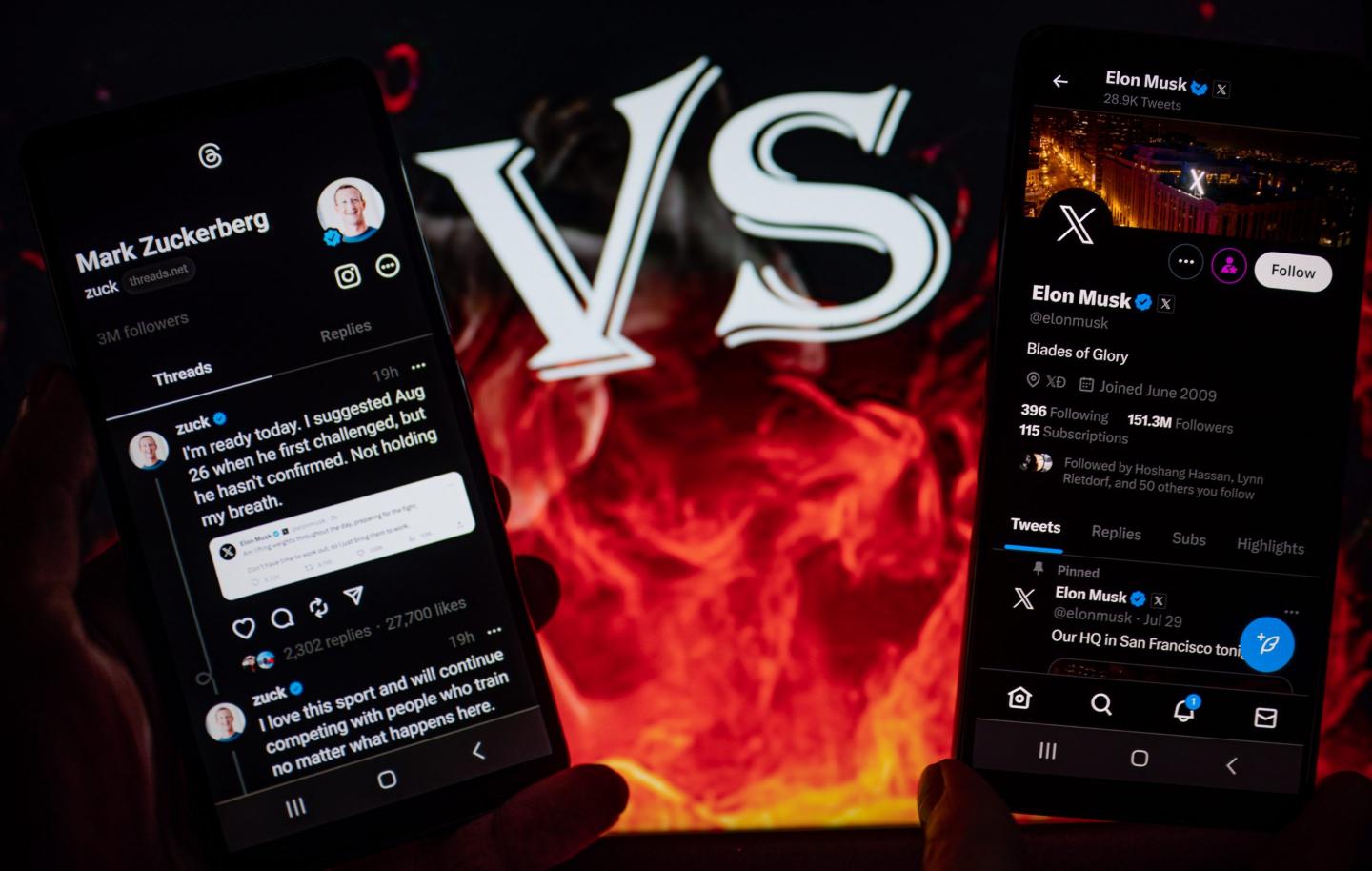 A picture of flames with VS in the middle of two iphones displaying Mark Zuckerberg's Threads profile and Elon Musk's Twitter profile