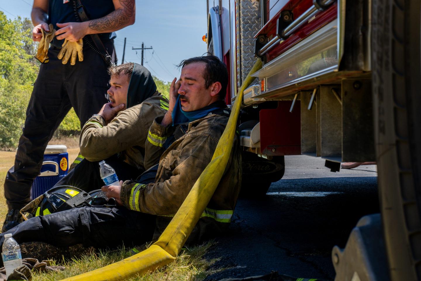 Three firefighters rest in the shade of a truck