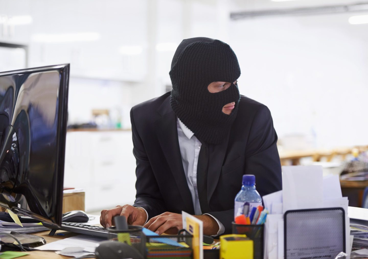 Shot of a hacker dressed in a black mask hacking a computer.