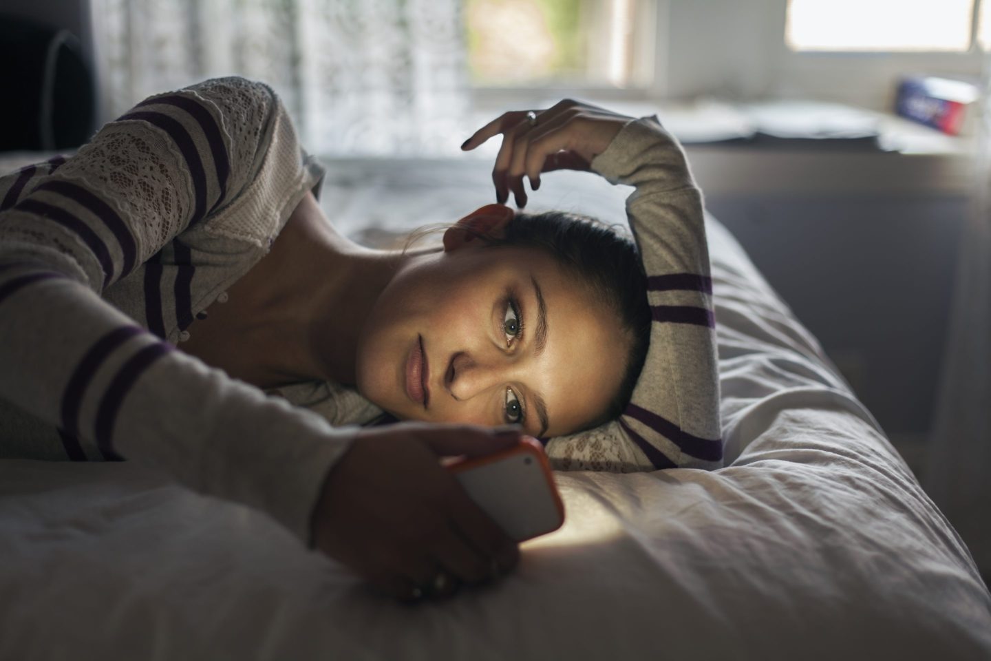 Young woman lying on her bed looking at a smartphone