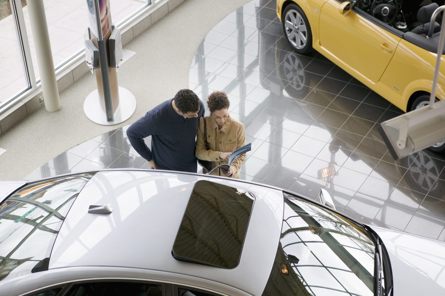 Two people comparing prices in a new car showroom