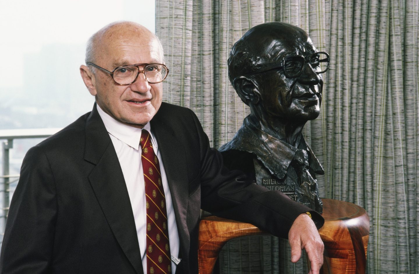Milton Friedman poses next to a bust of himself