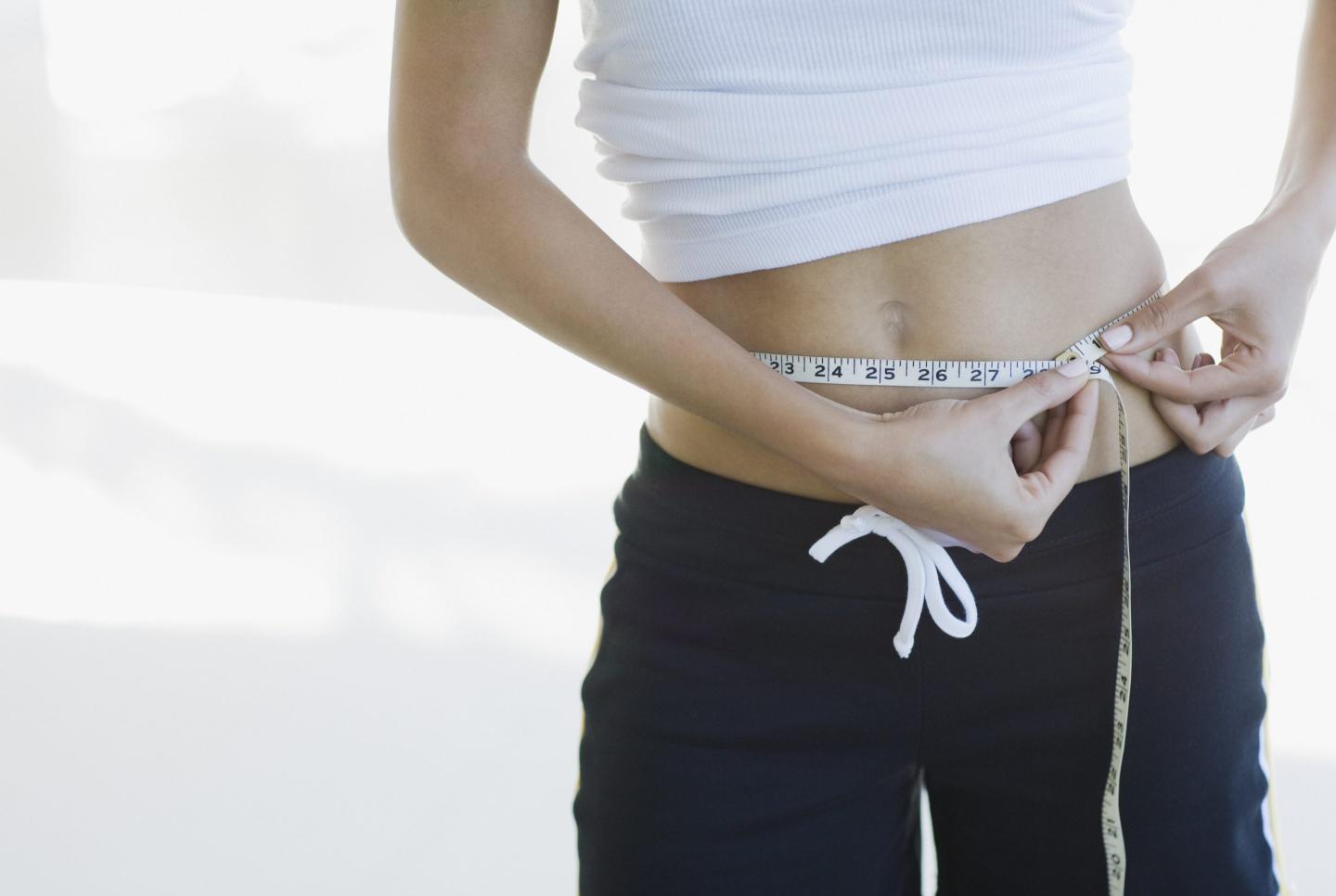 woman measuring her waist with a tape measure.