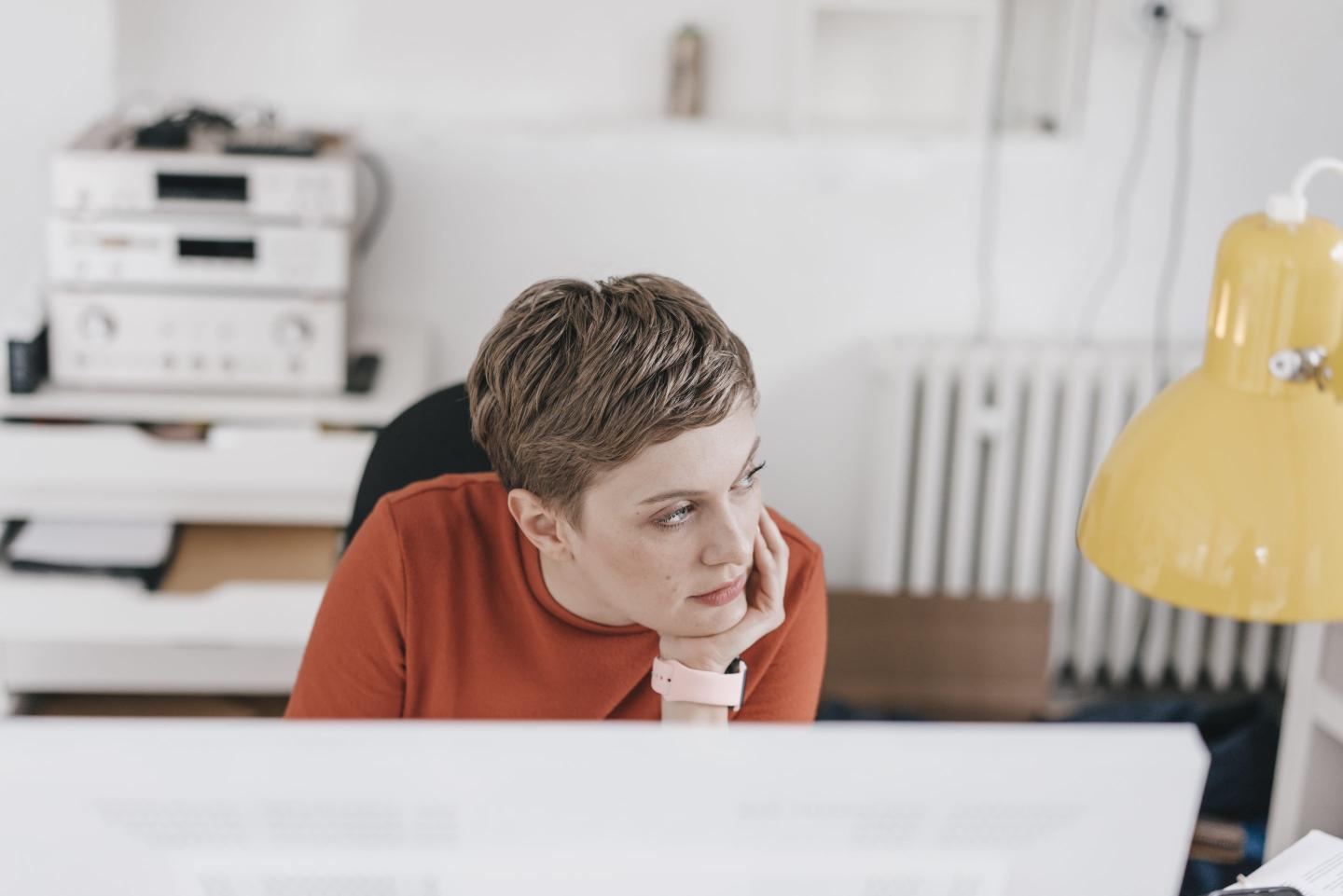 A woman sitting at a desk and looking off to her left with a bored expression.