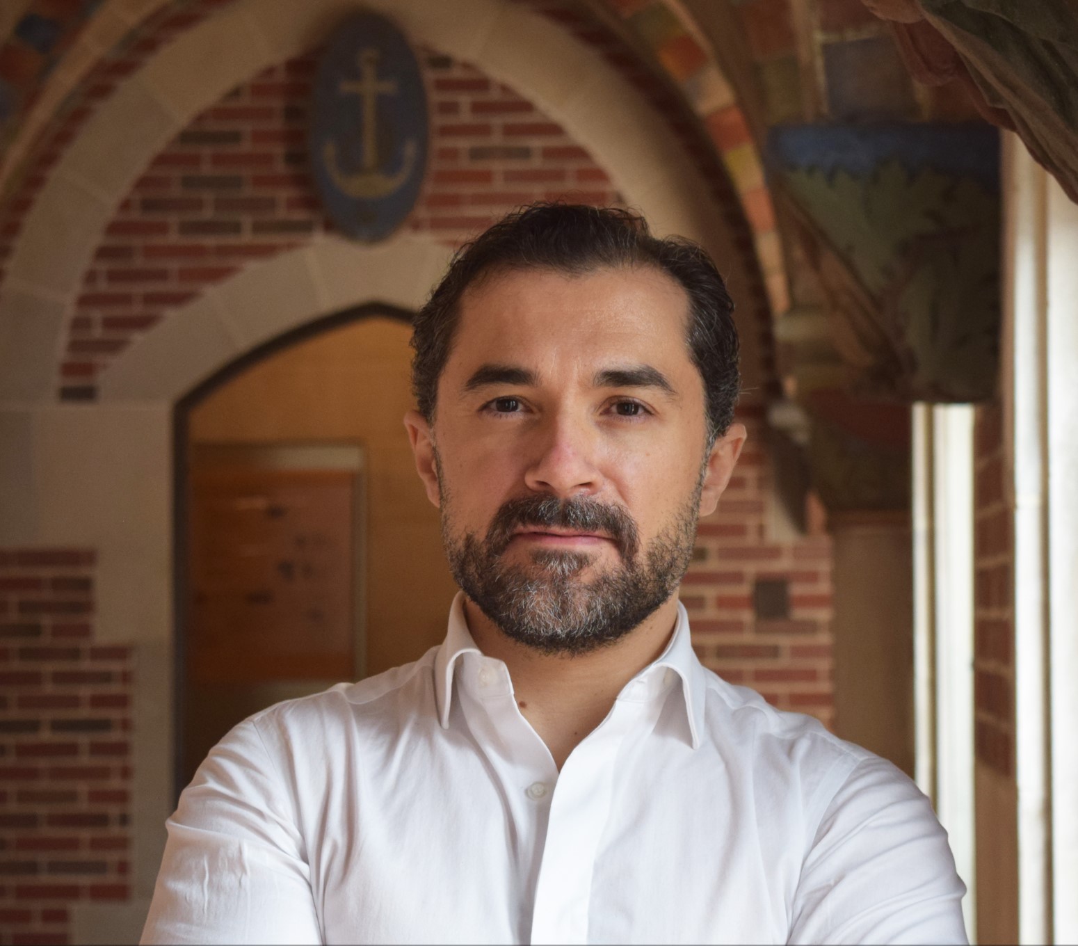 Professor stands with arms crossed in brick archway.