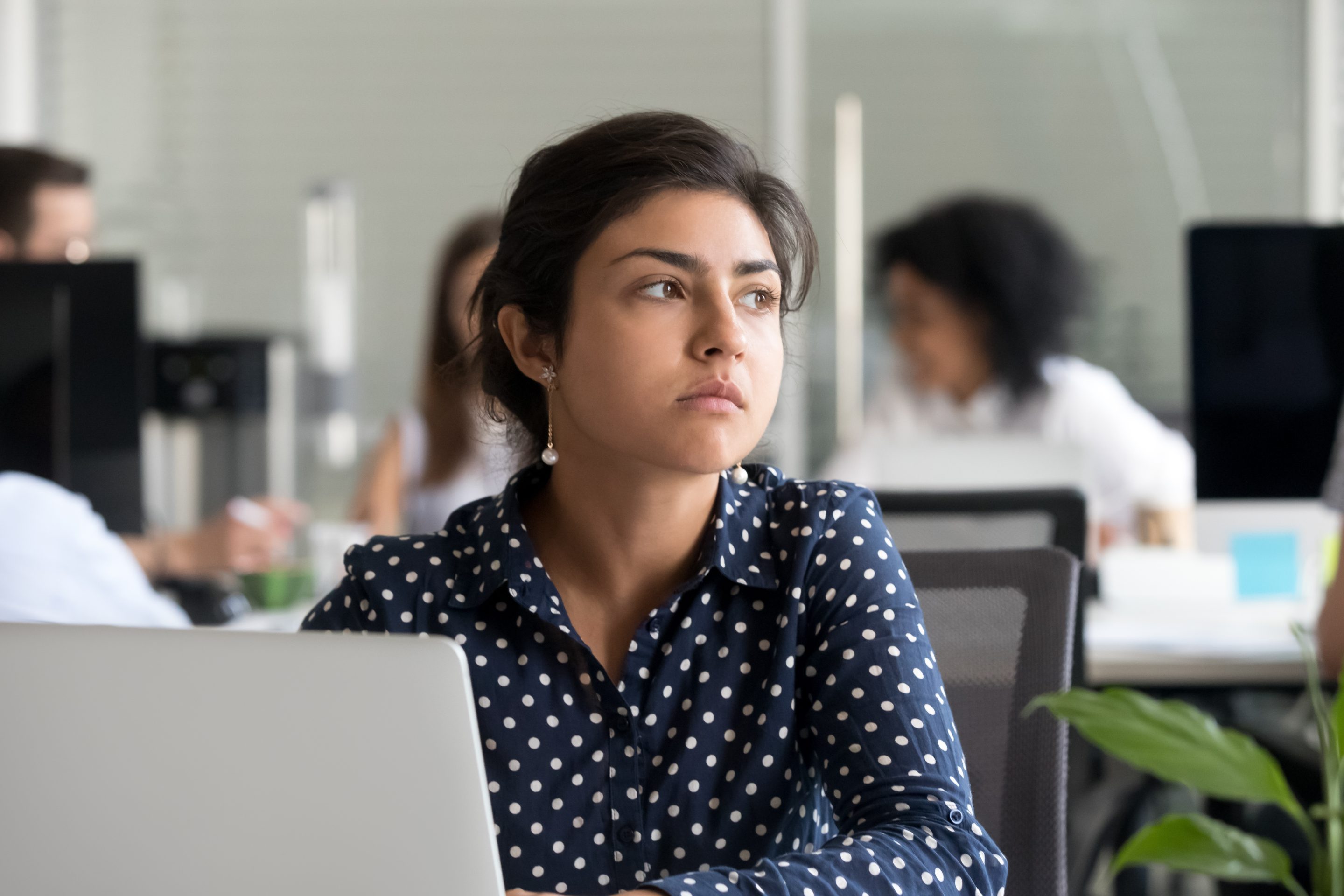 A woman in an office looks out of the window with a sad expression.