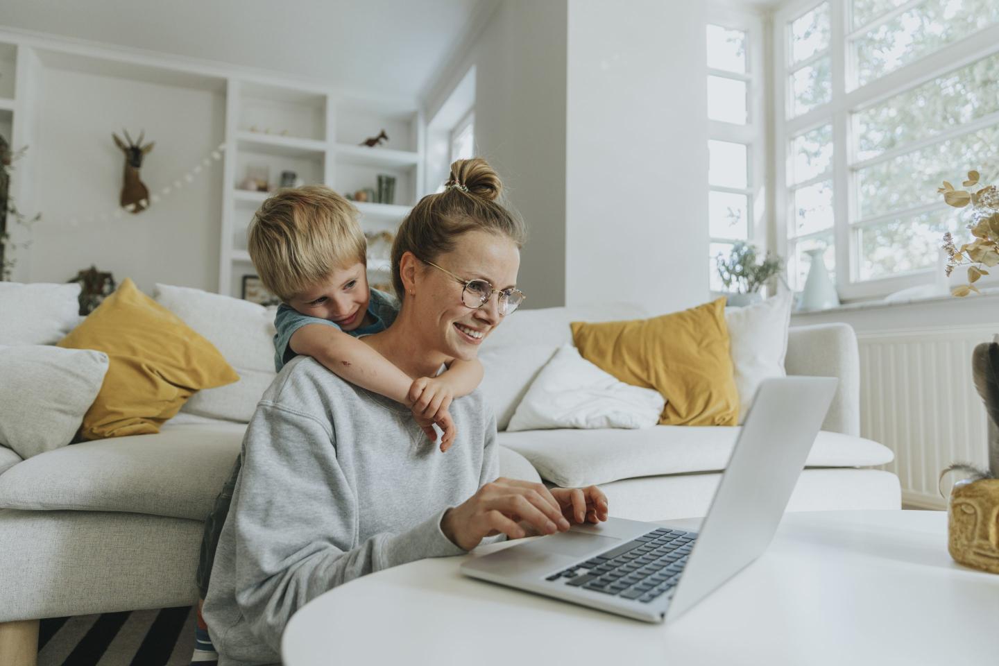 woman working at laptop with young boy hugging her