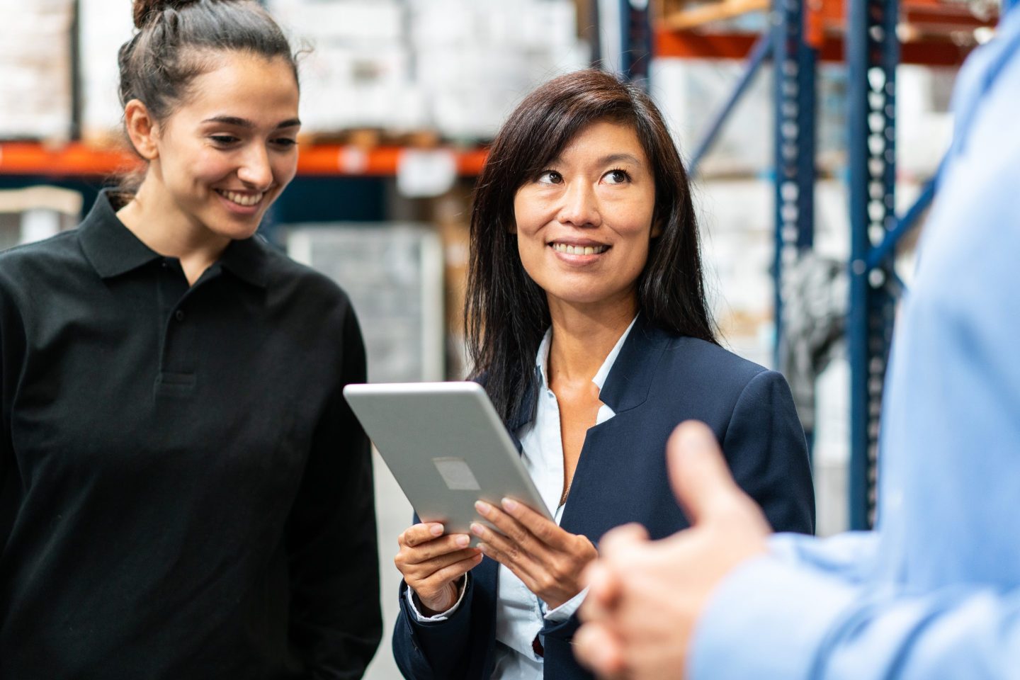 Smiling woman holding digital tablet having meeting with team in warehouse. Manager discussing and planning with warehouse team.
