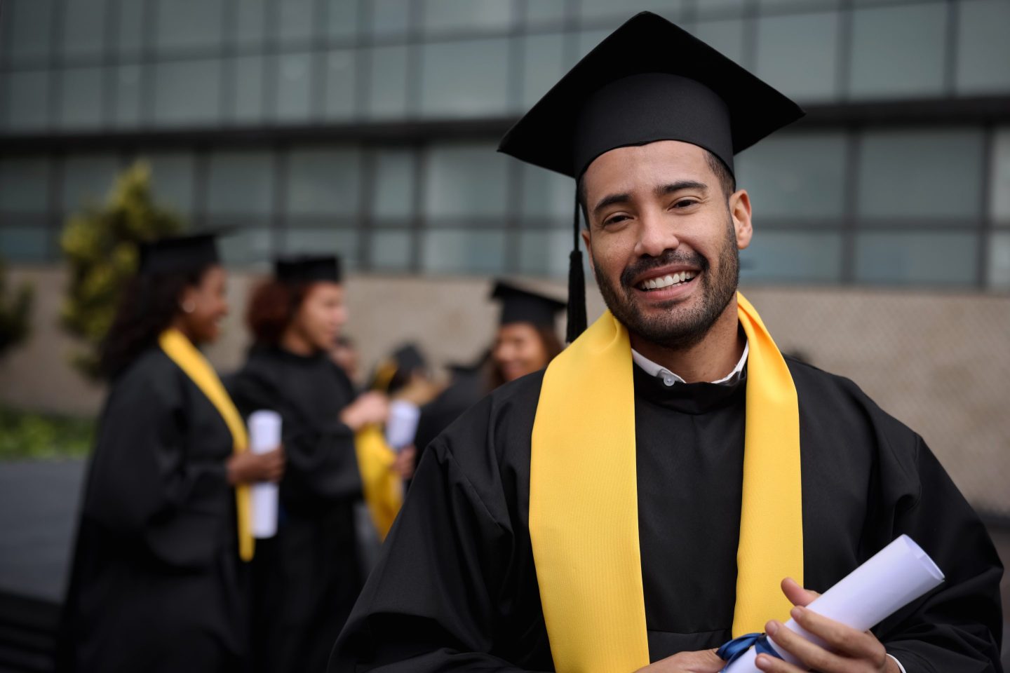 Portrait of a happy graduate student holding his diploma on graduation day and looking at the camera smiling.