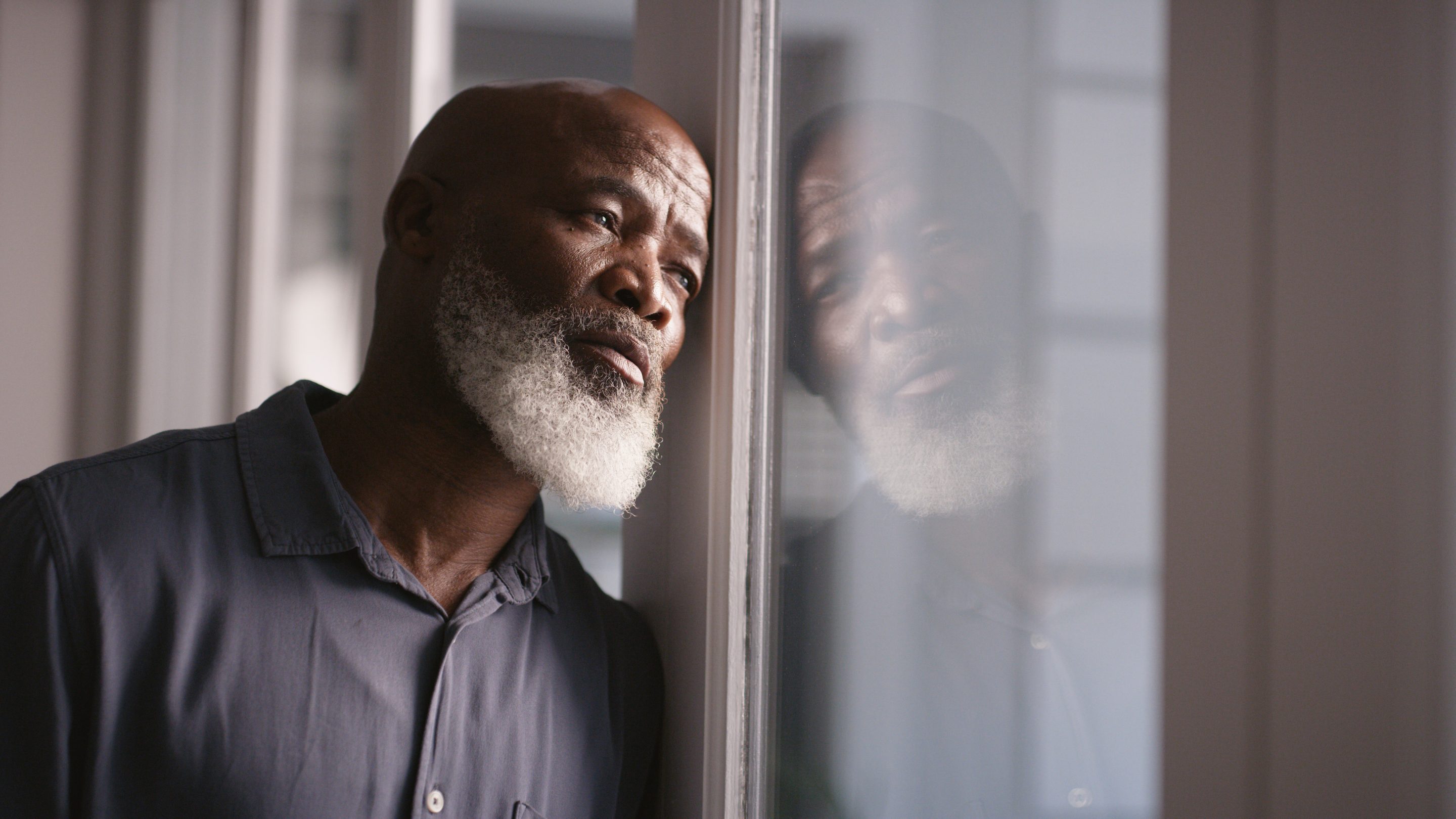 A man with a sad expression looks out a window.