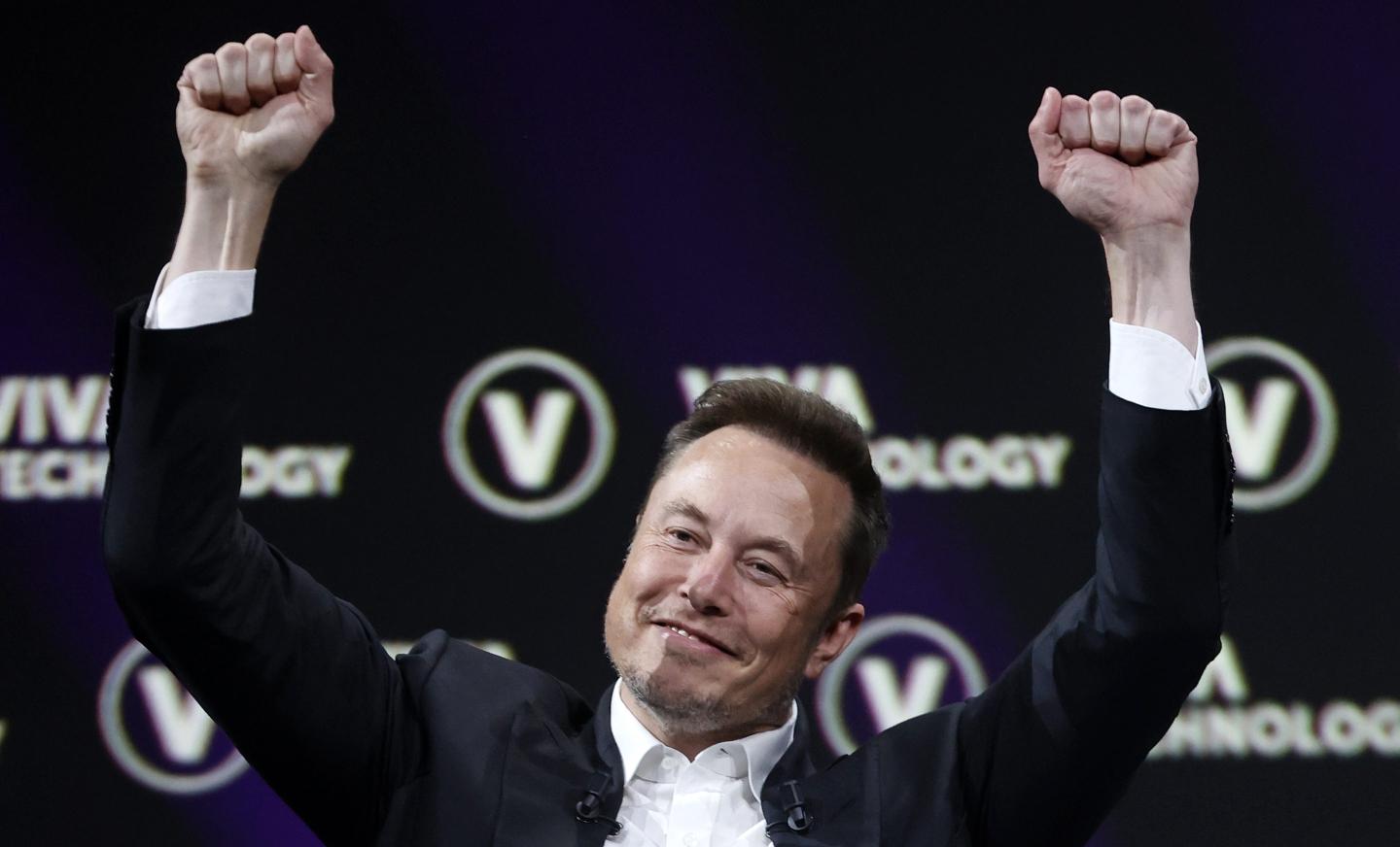Elon Musk smiling with his hands up in the air like he's celebrating.