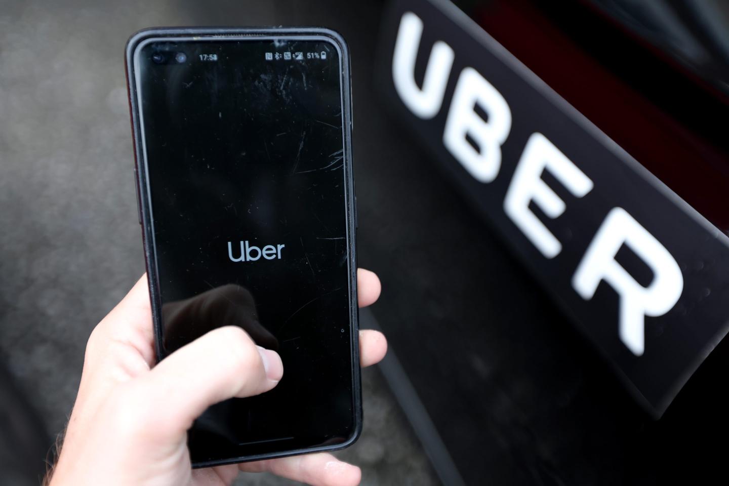 a picture of a person opening the uber app next to a cab with uber's logo