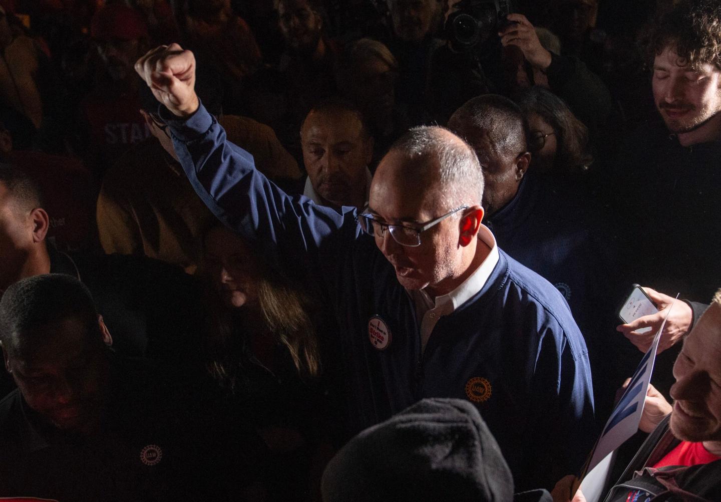 United Auto Workers union president Shawn Fain speaking to the media with his hand raised in a fist as a symbol of solidarity.
