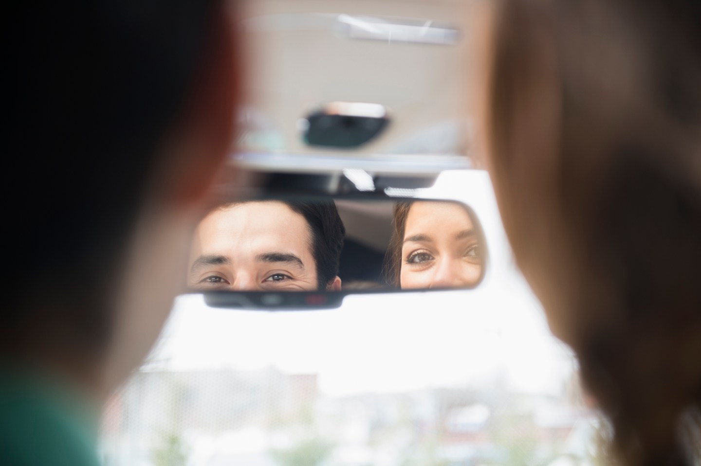A couple looks at themselves in a car's rearview mirror