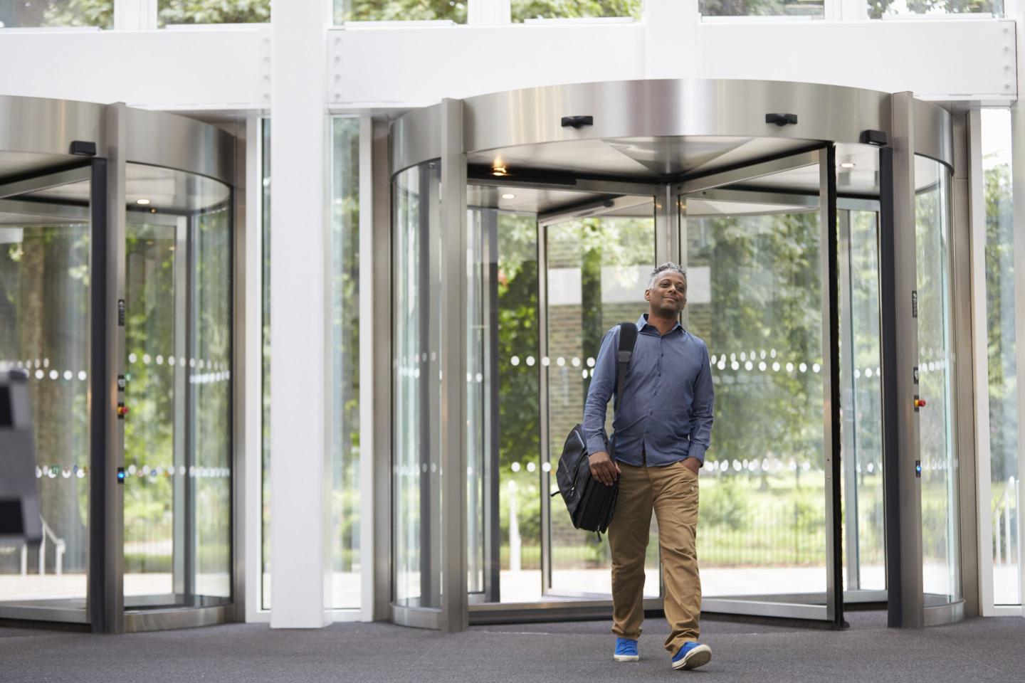 man with briefcase in professional clothing walks through the doors of an office building