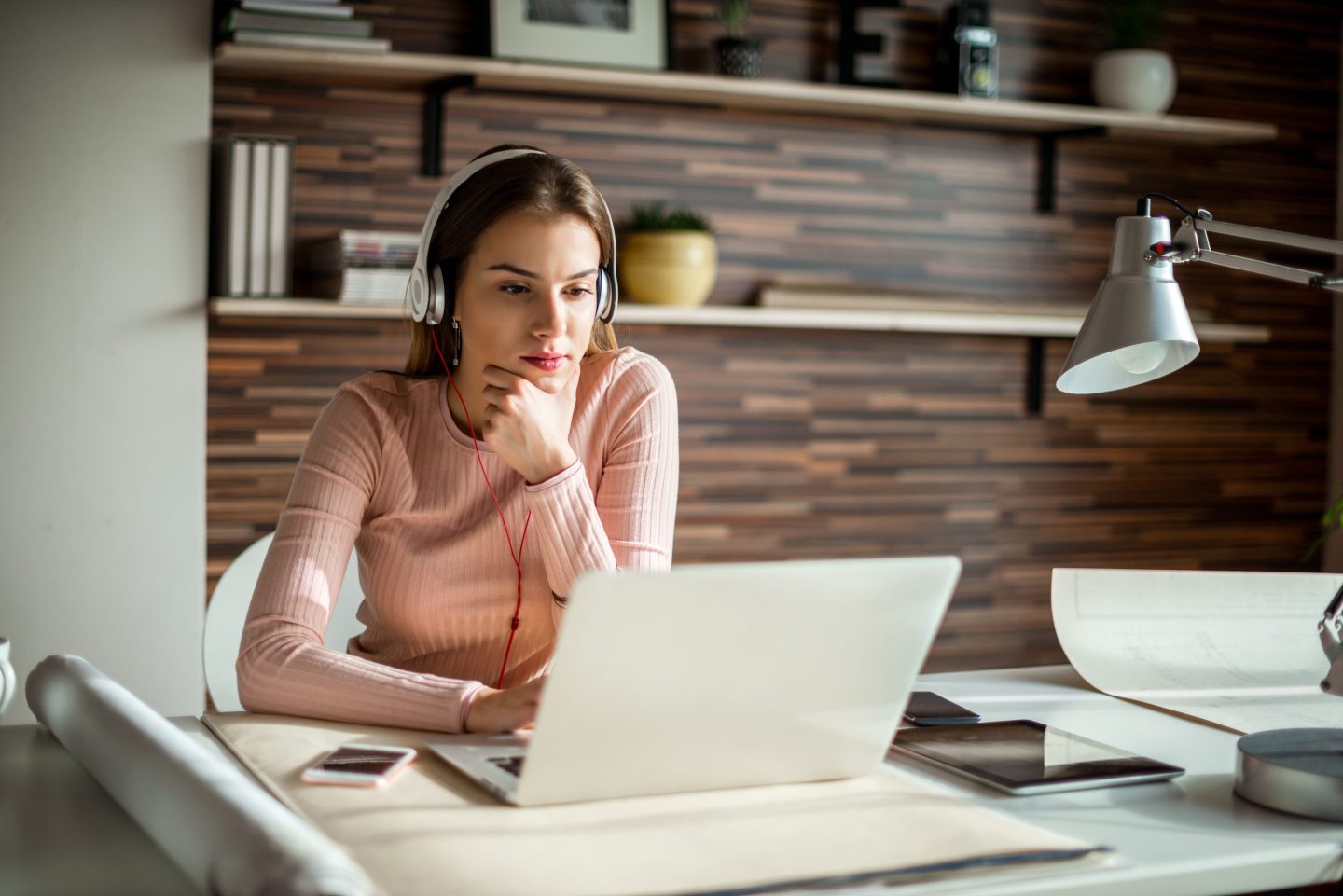 A woman wearing headphones works while using a laptop.