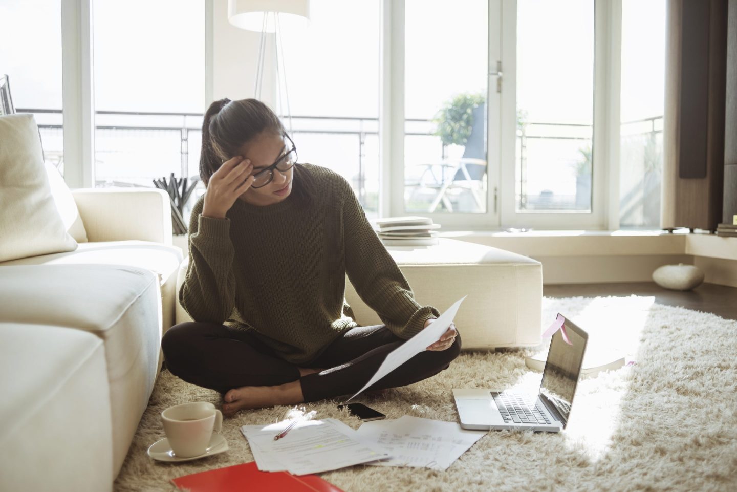 a person sitting on the floor with a hand on their forehead, papers and a laptop around them