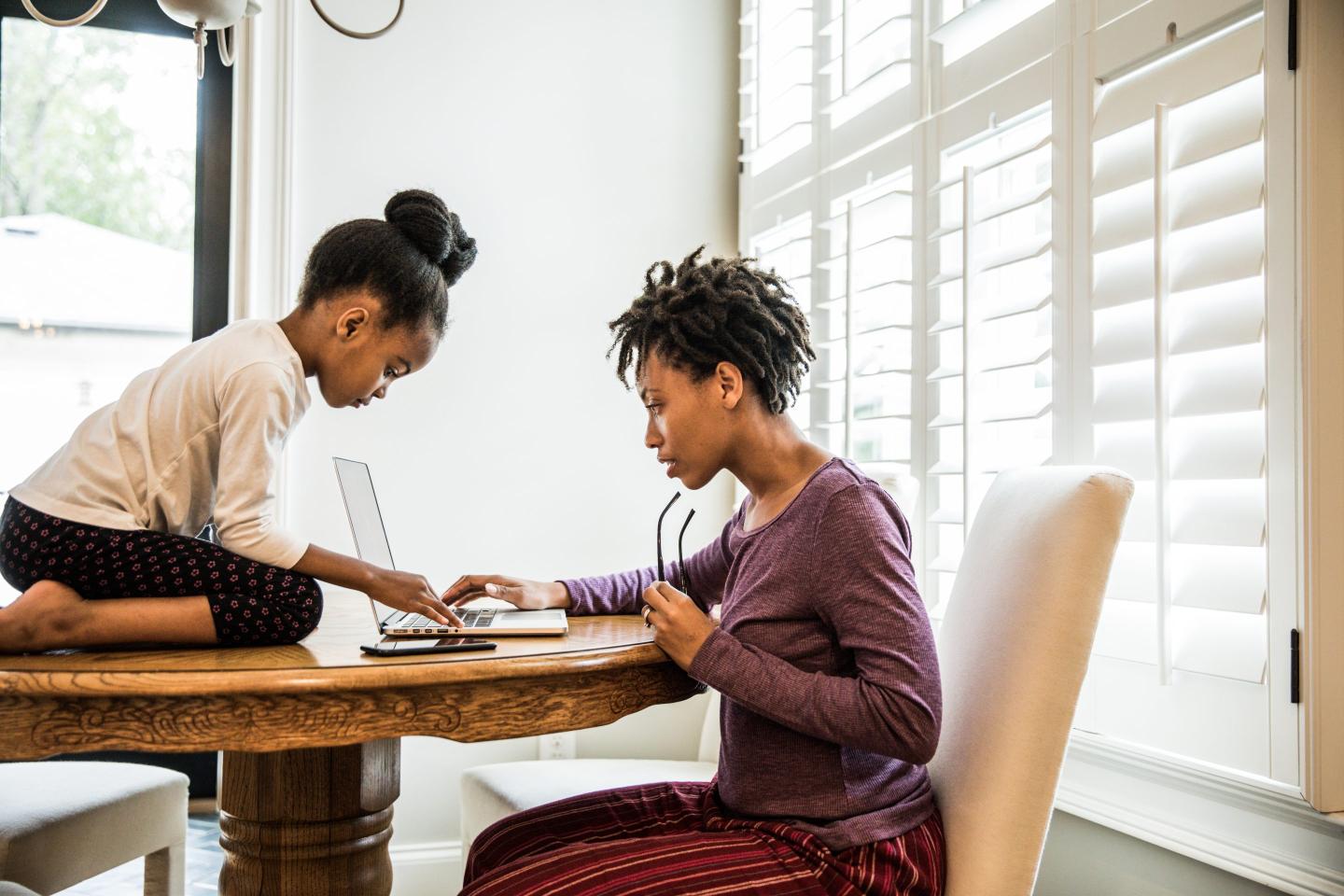Mother working on laptop, daughter on table