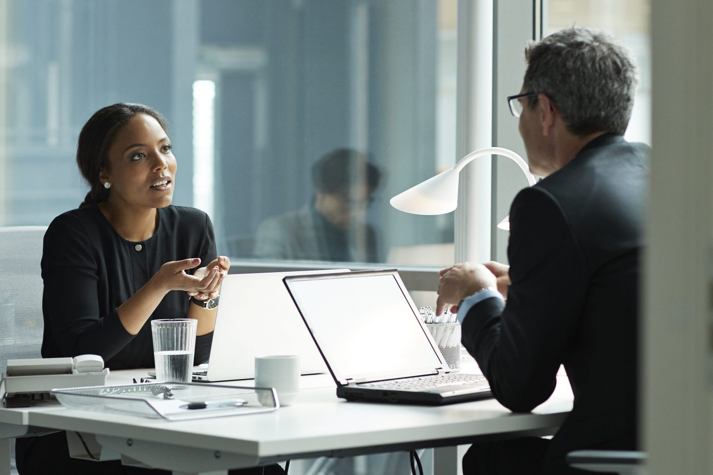 An executive woman speaks to another person at a desk