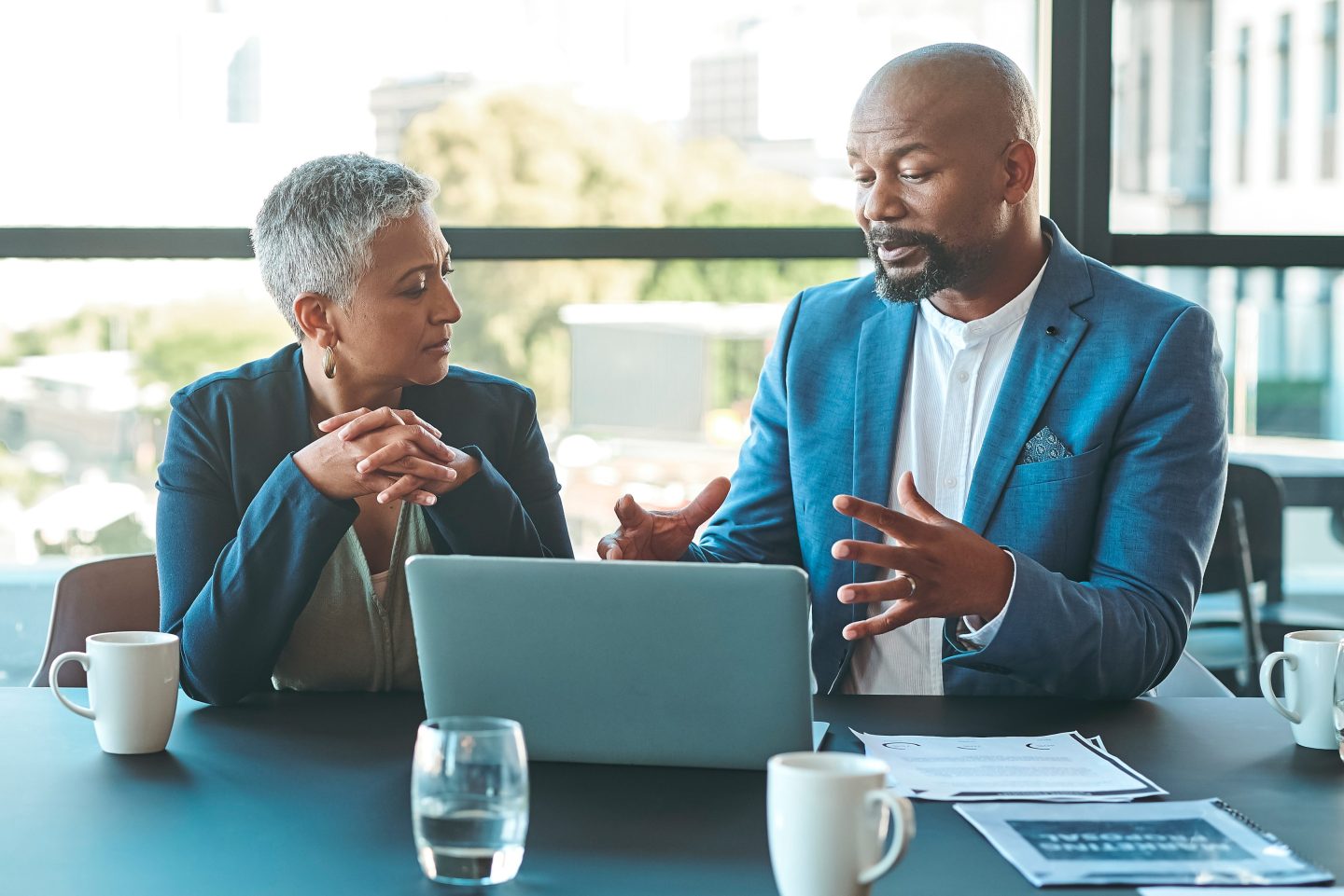 An older woman listens to a middle age man in a bright blue suit speak in front of a laptop