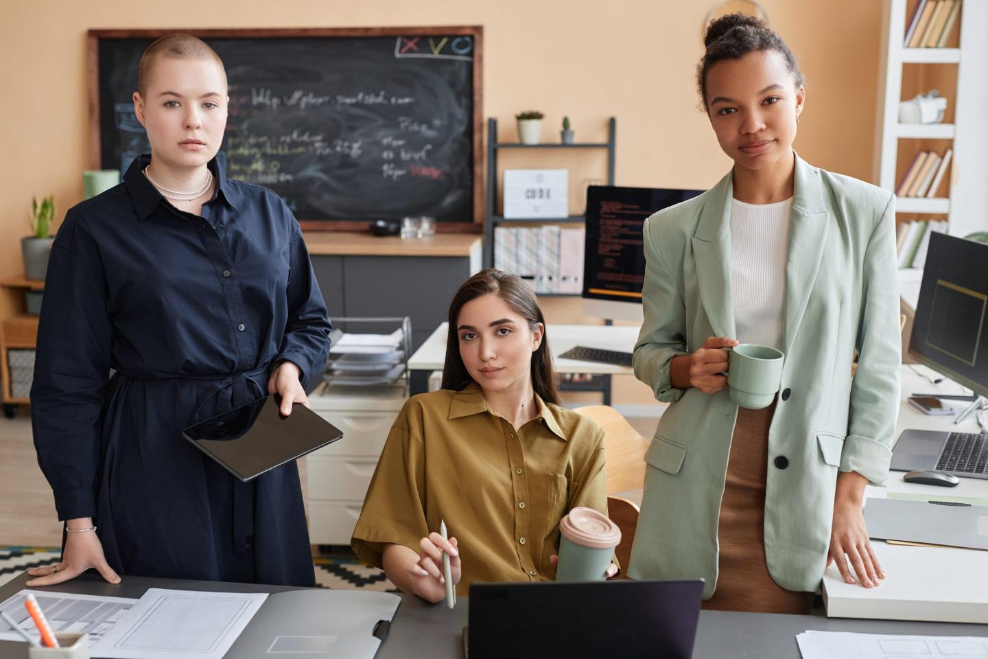 Three young women in business clothes look at the camera with serious expressions
