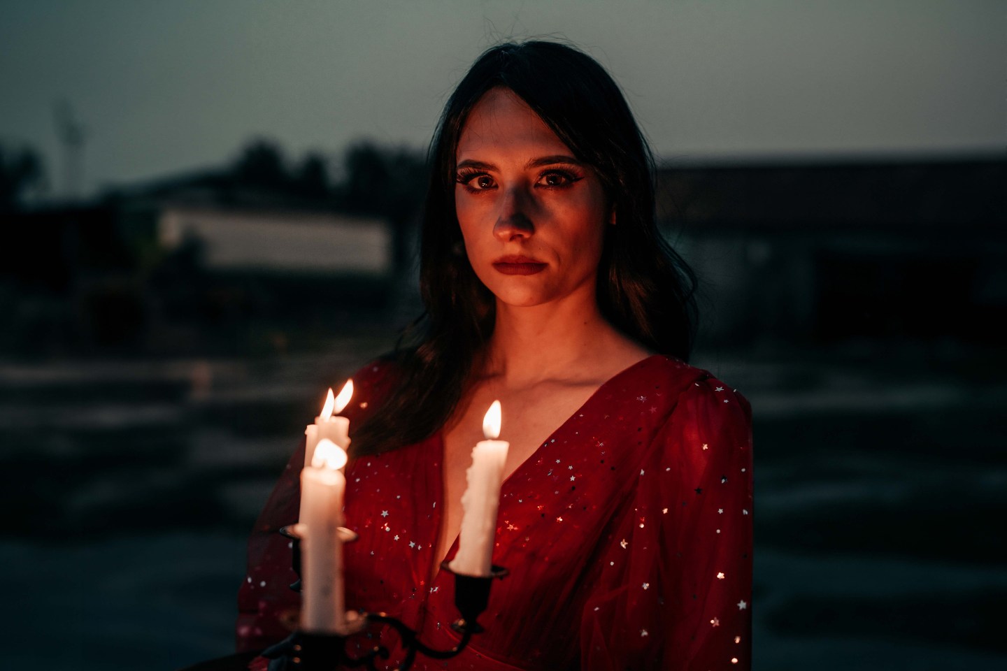 Chloe Hurst posed in a red dress holding a candelabra with lit candles that illuminate her face