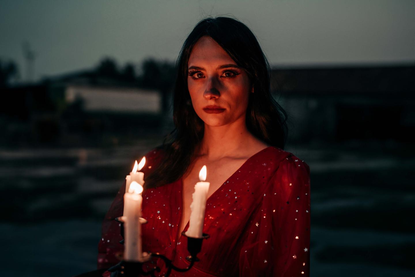 Chloe Hurst posed in a red dress holding a candelabra with lit candles that illuminate her face