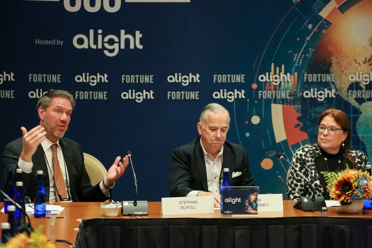3 adults sitting and speaking at a panel onstage