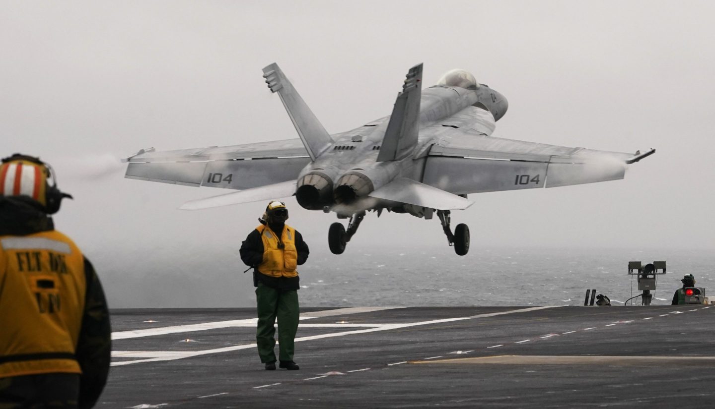 A military fighter jet is launched from the deck of the aircraft carrier.