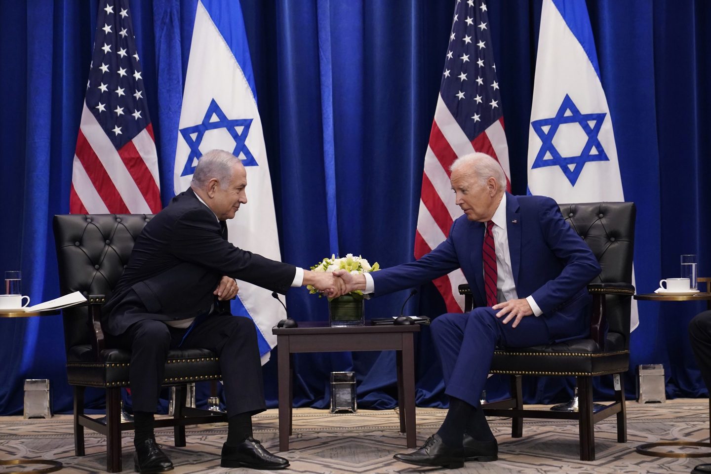 Israeli Prime Minister Benjamin Netanyahu and U.S. President Joe Biden shake hands with Israeli and American flags behind them