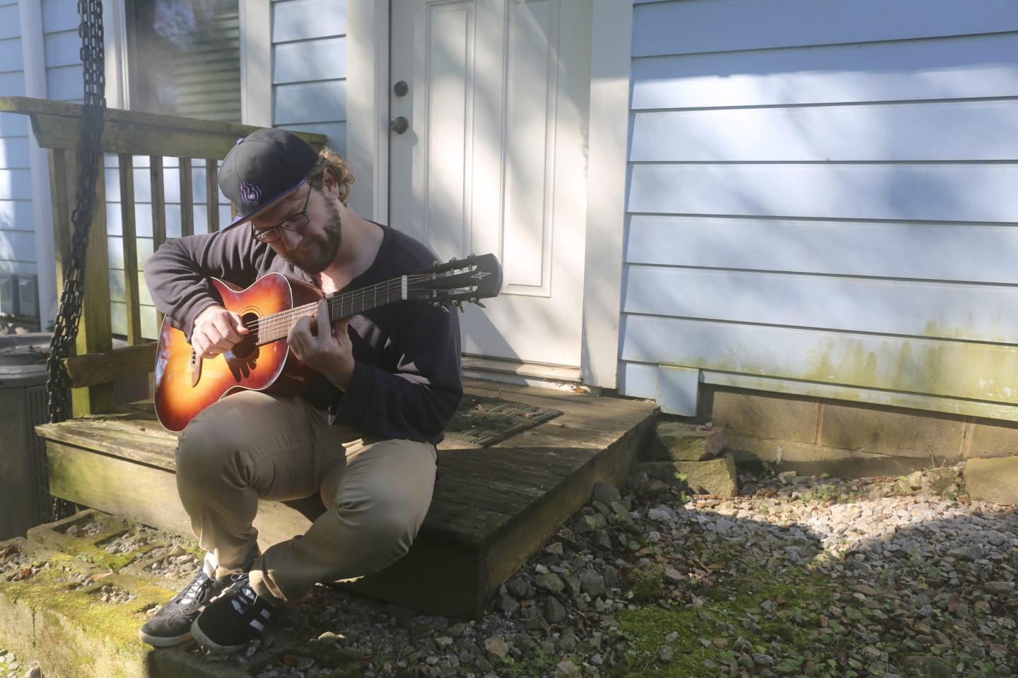 Man plays a guitar outside his apartment