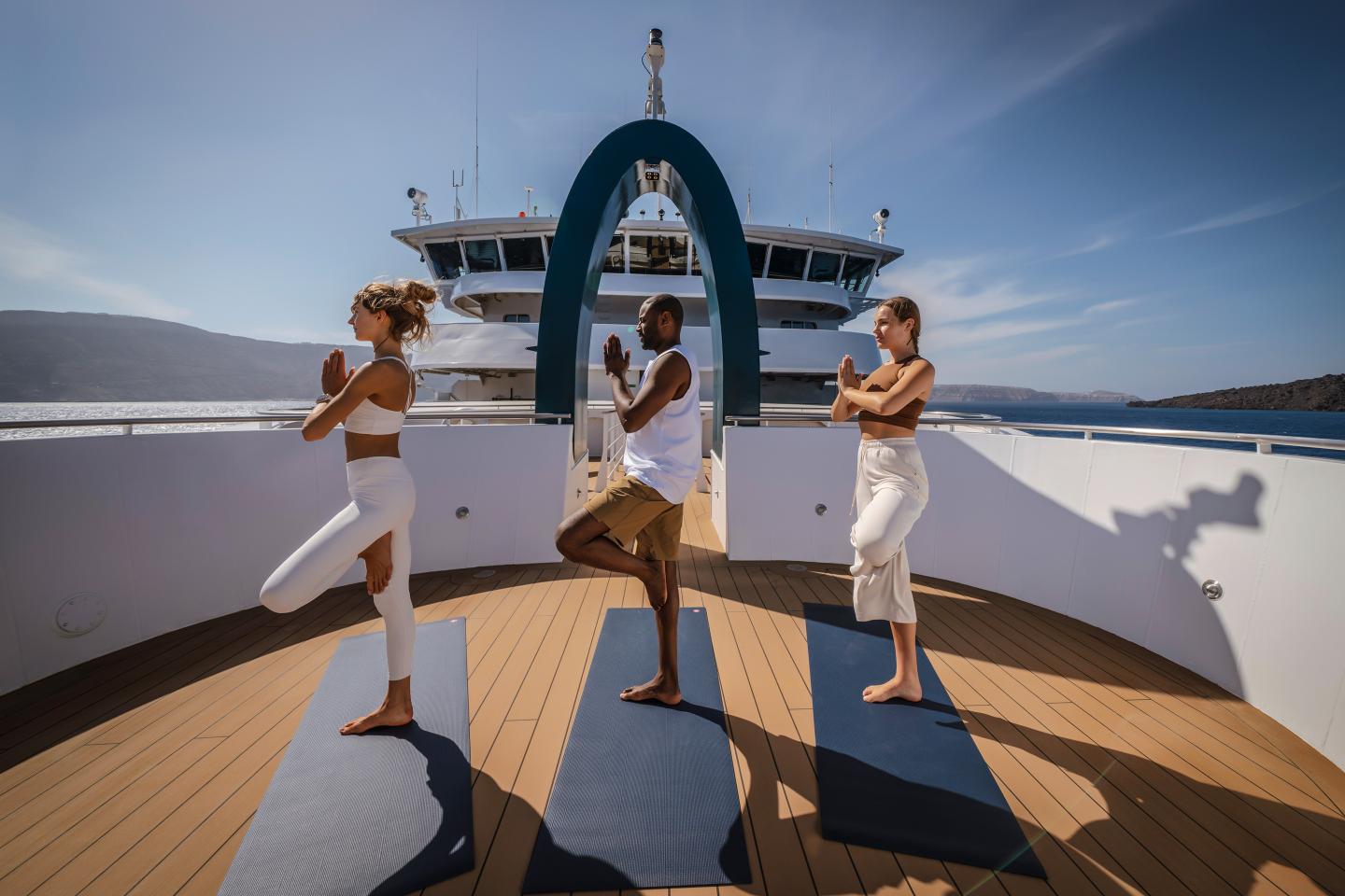 Three adults practicing yoga on the deck of a boat at sea.
