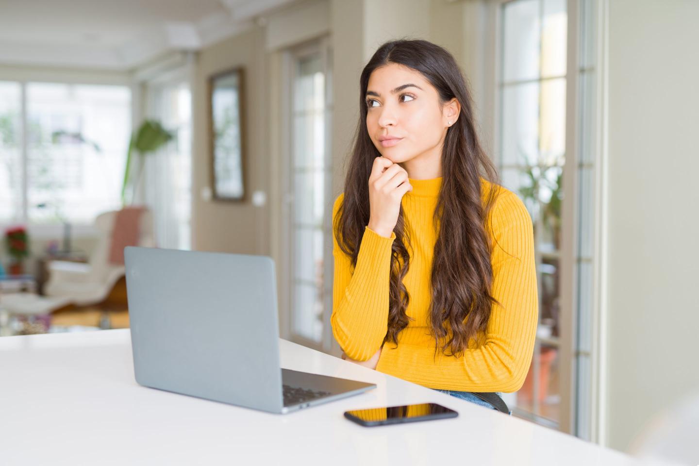 Young woman using computer laptop with hand on chin.