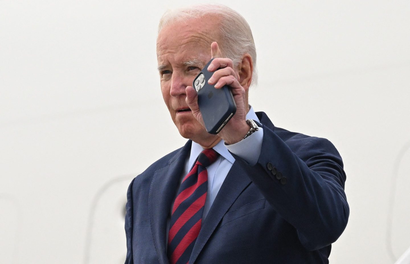 US President Joe Biden waves with his phone in his hand as disembarks from Air Force One