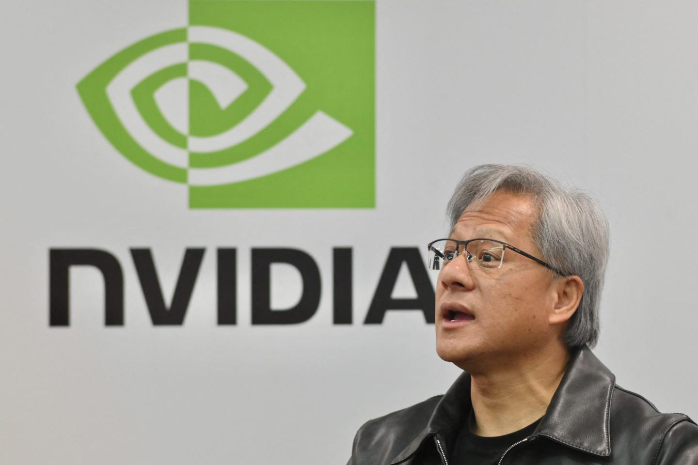 Nvidia CEO Jensen Huang speaks at a conference, with the company's logo on a backdrop behind him.