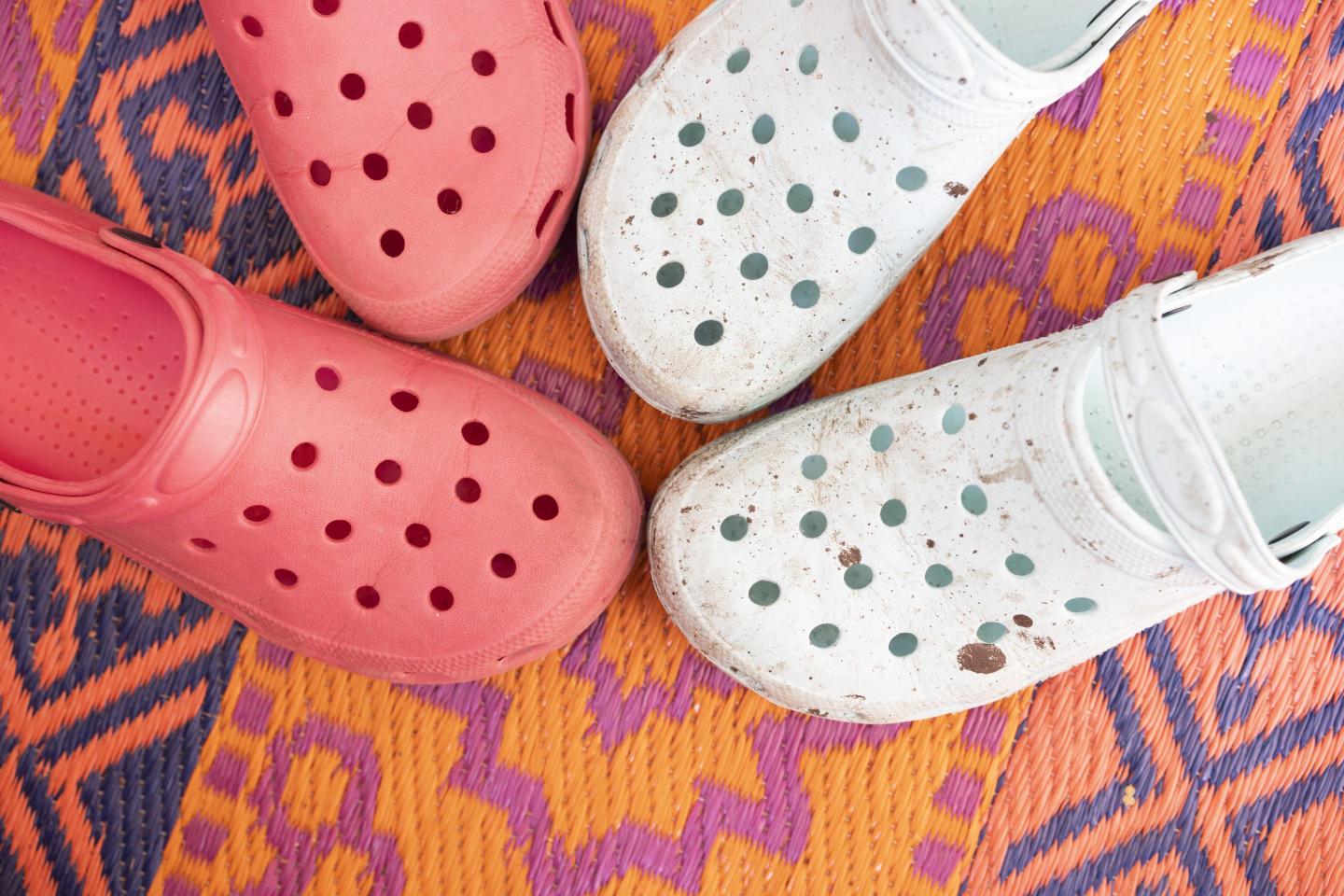 Two pairs of Crocs on a colorful carpet.