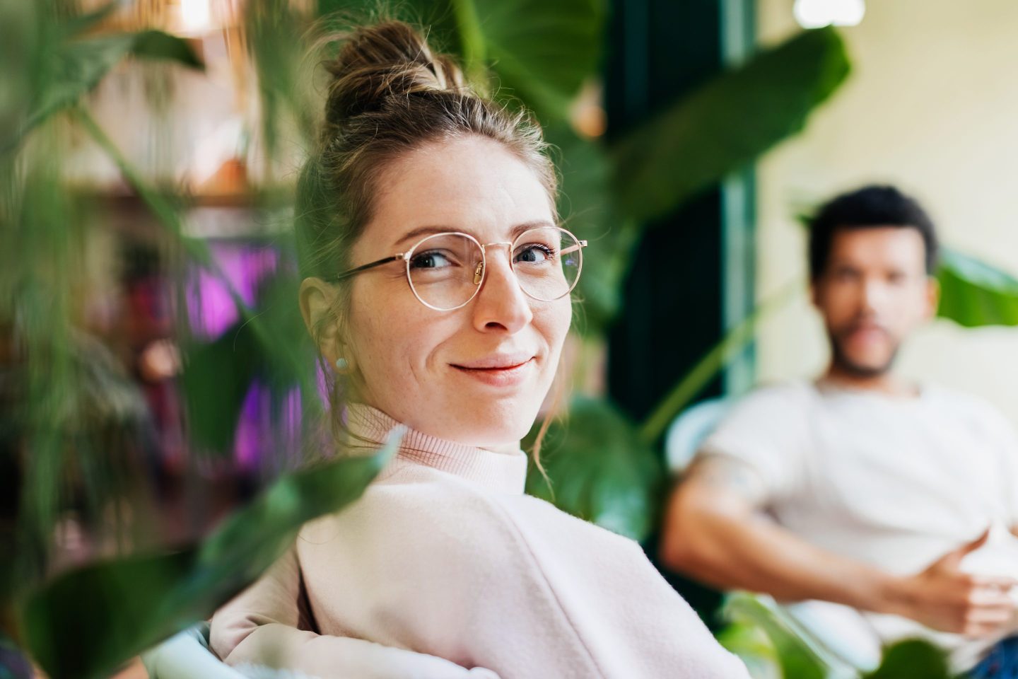 A portrait of a woman sitting between some green plants in a small café in the city.