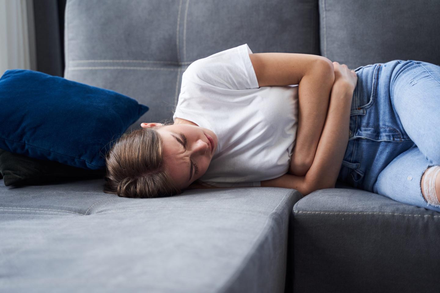 Woman lying on her side on a couch, holding her stomach in pain